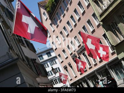 Schweizer Fahnen, die an Gebäuden in Zürich, Schweiz, an einem sonnigen Sommertag wehen. Stockfoto