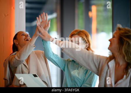 Drei fröhliche Geschäftsfrauen, die sich tagsüber im Büro zum Erfolg abklatschen Stockfoto