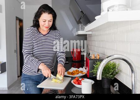 Frau schneidet frischen Salat während der Zubereitung eines hausgemachten Essens in einer modernen Küche Stockfoto