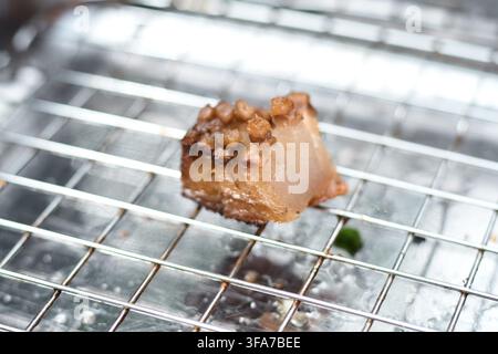 Eine Nahaufnahme eines herzhaften Stücks gebratenem Schweinebauch mit knuspriger Haut, das während der Zubereitung auf einem sauberen Metallgitter platziert ist. Stockfoto