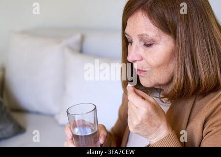 Seniorin, die zu Hause selbst mediziert, Altenpflege und Unabhängigkeit, eine Pille mit Wasser einnehmen. Konzept für häusliche Krankenpflege und Wohlbefinden, tägliche Routine für Stockfoto
