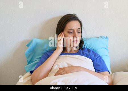 Heimpflege und Genesung, Frau mit Kopfschmerzen, die sich im Bett ausruht, Selbstpflege und Wohlbefinden zu Hause. Erwachsener Patient, der Schmerzen und Unbehagen erlebt, se Stockfoto