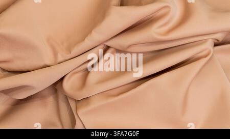 Eine Ansicht von oben einer hellbeigen Stoffoberfläche, die anmutig gefaltet ist, um sanfte, wellige Falten und eine glatte Textur zu enthüllen, Das warme, hellbraune Material Stockfoto