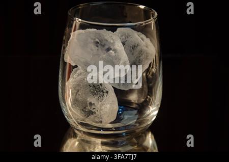 Klares Glas mit Eiswürfeln vor dunklem Hintergrund Stockfoto