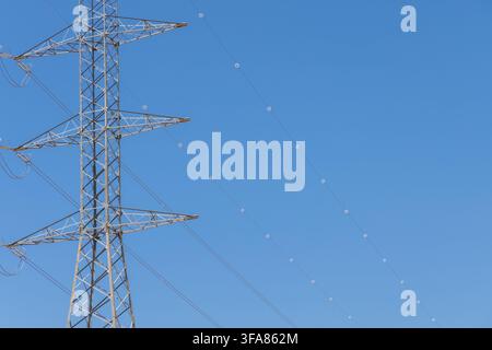 Eine Nahaufnahme eines Hochspannungsmastes mit seiner komplexen Gitterstruktur und den aufgehängten Kabeln, die sich über den Horizont erstrecken Stockfoto