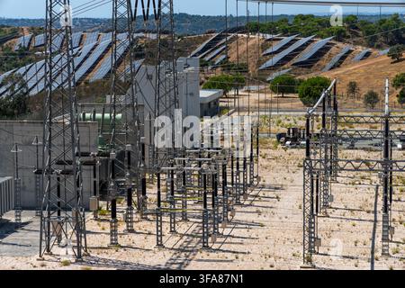 Reihen von Solarpanelen auf einem Hügel sind mit einer komplexen Umspannstation mit Hochspannungstürmen und Geräten verbunden Stockfoto