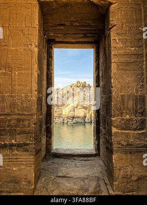 Ansicht eines antiken Steintors mit kunstvollen Hieroglyphenverzierungen, das einen malerischen Blick auf den Nil und die felsige Landschaft in Assuan, Aswan Gove einrahmt Stockfoto