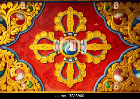 Ansicht eines farbenfrohen buddhistischen Vajra-Symbols, das in Relief in eine Tempelmauer geschnitzt ist, mit aufwendigen goldenen, roten und blauen Mustern in Pokhara, Gandaki Provi Stockfoto