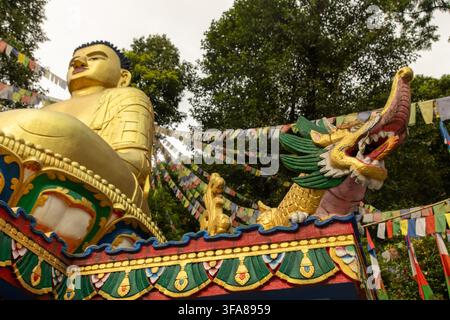Ansicht einer goldenen Buddha-Statue, geschmückt mit bunten Gebetsfahnen und einer dekorativen Drachenskulptur, in der Weltfriedens-Pagode in Pokhara, Gandaki-Provinz Stockfoto