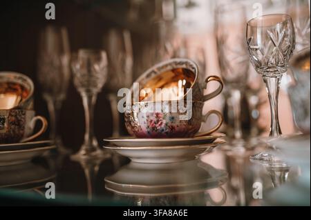 Nahaufnahme eines Porzellan-Teeservices, das neben Kristallgläsern ausgestellt ist. Antikes Geschirr und traditionelles Wohninterieur. Stockfoto
