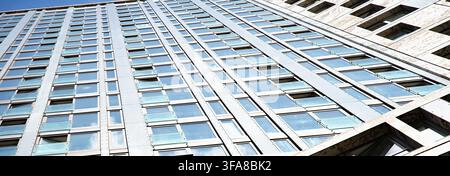 Eine auffällige moderne Gebäudefassade mit sauberen Fenstern und einer schlanken Metallstruktur, vor einem lebendigen blauen Himmel in einer städtischen Umgebung. Erfasst von Stockfoto