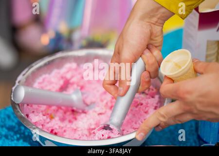 Rosa Frucht-Eiscreme Gelato, serviert in einer Edelstahl-Mischschüssel mit zwei metallischen Eiscreme-Scoop Stockfoto