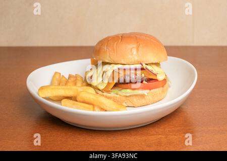 Cheeseburger mit roter Zwiebel, Tomate und Senfsauce, serviert mit dick geschnittenen Pommes auf weißem Teller Stockfoto
