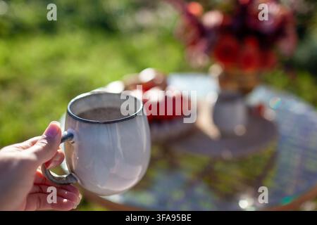 Heißer, dampfender Morgenkaffee im herbstlichen Garten neben einem Strauß Herbstblumen trinken. Nahaufnahme der Tasse in den Händen im Freien. Frau entspannt sich mit ihrem Getränk. Stockfoto