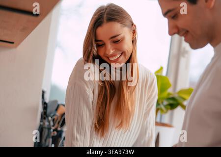 Lächelnde junge Frau teilt einen fröhlichen Moment mit ihrem Partner in einer hellen modernen Hausküche Stockfoto