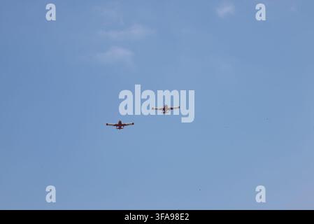 Zwei rot- und weißfarbene Propellflugzeuge fliegen in Formation durch einen klaren blauen Himmel Stockfoto