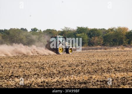Nahaufnahme Rückansicht eines modernen grünen Traktors, der trockenen Ackerboden bearbeitet und eine große Staubwolke aufwirbelt. Stockfoto