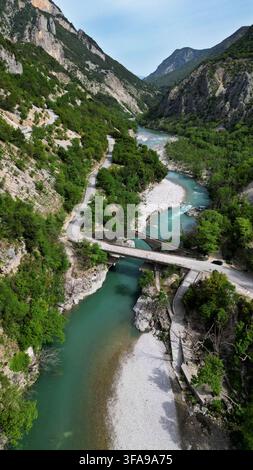 Spektakulärer vertikaler Drohnenaufnahm von einer historischen Steinbögenbrücke und einer modernen Straße über einen wilden türkisfarbenen Fluss. Schöne landschaftliche Schlucht mit grü Stockfoto