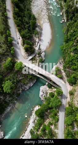 Spektakulärer vertikaler Drohnenaufnahmeblick von oben auf Brücken, die einen wilden türkisfarbenen Gebirgsfluss kreuzen. Szenische Schluchtlandschaft mit einer sich windenden Asphaltstraße, par Stockfoto
