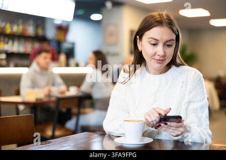 Junge Frau, die im Café sitzt und auf dem Handy plaudert Stockfoto