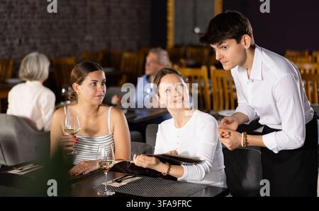 Junger männlicher Kellner, der von zwei Frauen im Restaurant bestellt wird Stockfoto