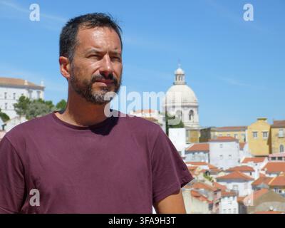 Ein schlanker, dunkelhaariger, weißer europäischer Mann mit gestutztem Bart trägt ein burgunderrotes T-Shirt und entspannt sich in Lissabon, Portugal. Stockfoto