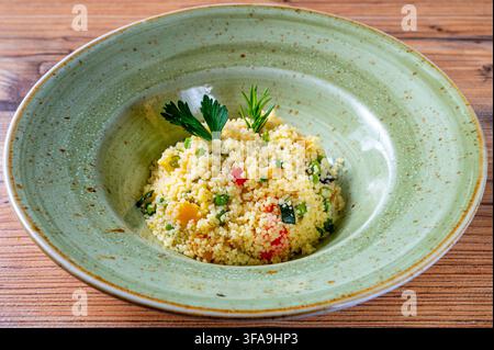 Gemüse-Couscous mit Erbsen, Zucchini und buntem Gemüsemischung, garniert mit frischer Petersilie und Rosmarin und serviert in einer rustikalen Keramikschale Stockfoto
