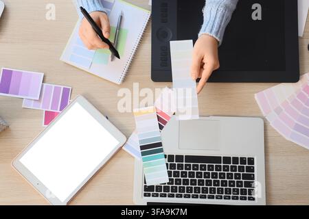 Grafikdesigner und kreativer Workflow-Designer arbeitet mit Farbpaletten, Laptop und Tablet auf einem Holztisch Stockfoto