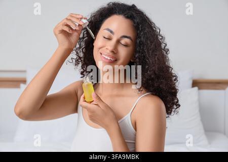 Haarpflege und Schönheitsroutine, glückliche junge Frau, die natürliches Ölserum auf ihr lockiges Haar zu Hause aufträgt Stockfoto