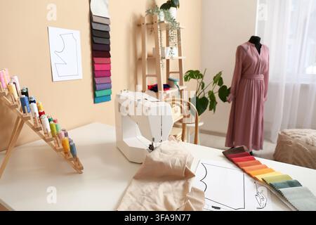 Nähmaschine mit Stoff, Garnspulen und Stoffmustern auf dem Schneiderisch im Atelier Stockfoto