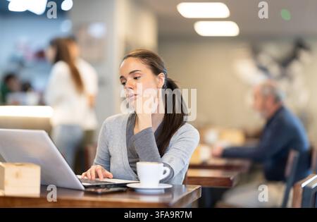 Die Europäerin sitzt an einem Tisch in einem Café und arbeitet an einem Laptop. Stockfoto