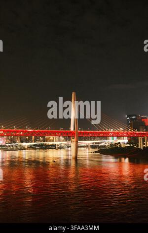 Beleuchtete Dongshuimen-Brücke über den Jangtsekiang bei Nacht mit roten Lichtern, die sich auf dem Wasser spiegeln, Chongqing, China. Stockfoto