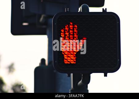 Rotes Handsignal leuchtet hell an der Ampel. Signal warnt Fußgänger, das Überqueren der Straße einzustellen. Klarer Himmel als Hintergrund betont die Dringlichkeit des Zeichens. Ideal Stockfoto