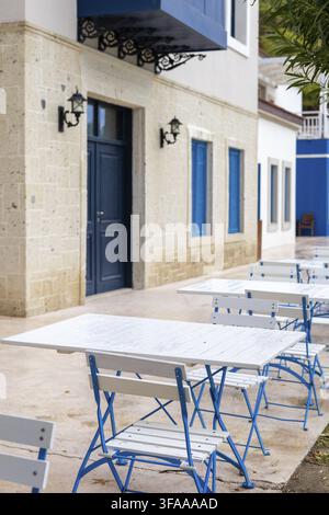 Blau-weiße Tische und Stühle sind ordentlich in einem Essbereich im Freien mit blauen Akzenten und weißen Möbeln angeordnet. Perfekt, um eine Mahlzeit zu genießen Stockfoto