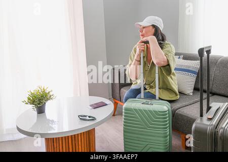 Reife Reisende, die sich auf den Griff ihres Koffers lehnt, während sie auf die Abreise wartet Stockfoto