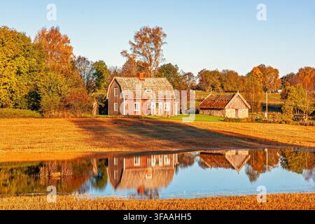 Bauernhaus und Scheune spiegeln sich in einem ruhigen ländlichen Teich auf einem Feld im Herbst Stockfoto
