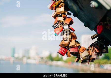 Liebes Schlösser, die an der Eisernen Steg-Fußgängerbrücke über den Main in Frankfurt am Main, Deutschland, befestigt sind, mit der verschwommenen Stadtuferlandschaft im Stockfoto
