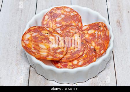 Nahaufnahme von scharfen italienischen Salamischeiben, die in einer geriffelten weißen Schale auf einem Holztisch gestapelt sind. Stockfoto