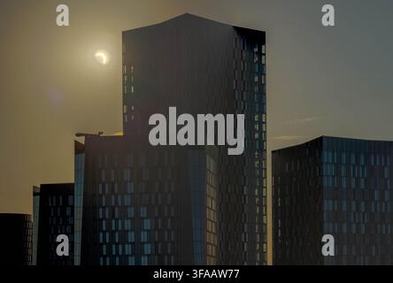 Nahaufnahme mit Teleobjektiv der partiellen Mondsichel-Sonnenfinsternis am Himmel neben dem South-Tower-Wolkenkratzer am Deansgate Square in Manchester. Stockfoto