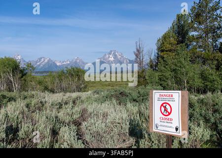 Grand Teton National Park, WY, USA – 26. Juni 2026: Warnschild, das ein Gebiet für Besucher aufgrund von Bärenaktivität mit Salbeigestrüpp und schneebedeckten Teton-Bergen sperrt Stockfoto