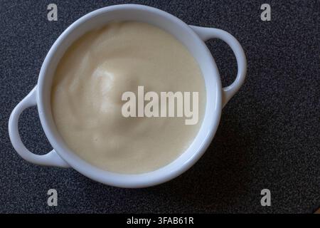 Ansicht von oben: Hausgemachte italienische Zabaione, ein geschlagener Eigelb-Marsala-Wein-Pudding in einer weißen Keramikschale mit zwei Henkeln vor dunklem Hintergrund Stockfoto