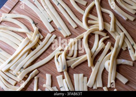 Ansicht von oben über frisch zubereitete Scialatielli, eine traditionelle italienische Pasta mit Basilikumflecken auf einem Holzmesserbrett Stockfoto