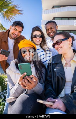 Gruppe von Freunden, die zusammen im Freien in einer sonnigen Nachbarschaft Smartphones nutzen Stockfoto