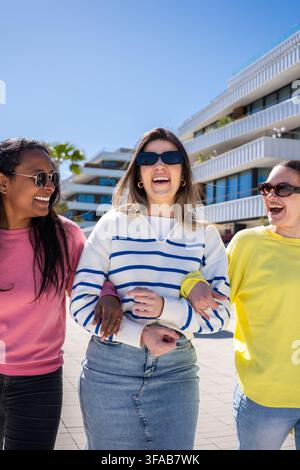 Drei Freundinnen gehen und lachen im Freien an einem sonnigen Tag Stockfoto