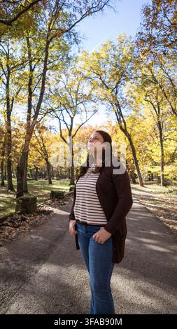 Frau, die auf einem Waldweg innehält und die sich verändernden Blätter im Herbst schätzt Stockfoto