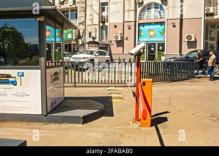 Batumi, Georgien - 19. Juli 2026: Automatisches Parkplatzschranke mit Kabine, Sicherheitskamera und Geschwindigkeitshügel auf einer sonnigen Stadtstraße in der Nähe einer Gebäudefassade. Stockfoto