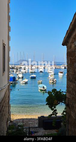 Scenische Aussicht durch eine enge Passage mit Blick auf einen sonnenbeschienenen Hafen mit festgemachten Booten in Hvar, Kroatien. Stockfoto