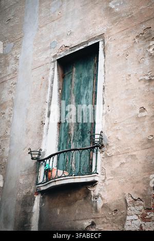 04. Oktober 2022: Blick auf eine gealterte, verwitterte Gebäudefassade mit einem hohen, schmalen Fenster mit abblätternden grünen Holzläden und einem verzierten Schmiedeeisen Stockfoto