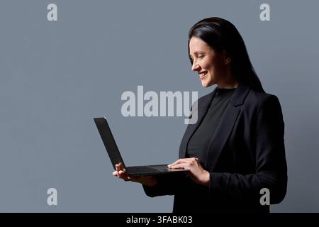 Lächelnde Geschäftsfrau, die einen Laptop verwendet, Seitenansicht im Studio Stockfoto