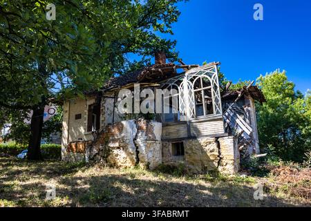 Verlassenes und stark verfallenes altes Haus in Serbien mit eingestürztem Dach, einst eine luxuriöse kleine Villa, jetzt umgeben von überwucherter Vegetation Stockfoto